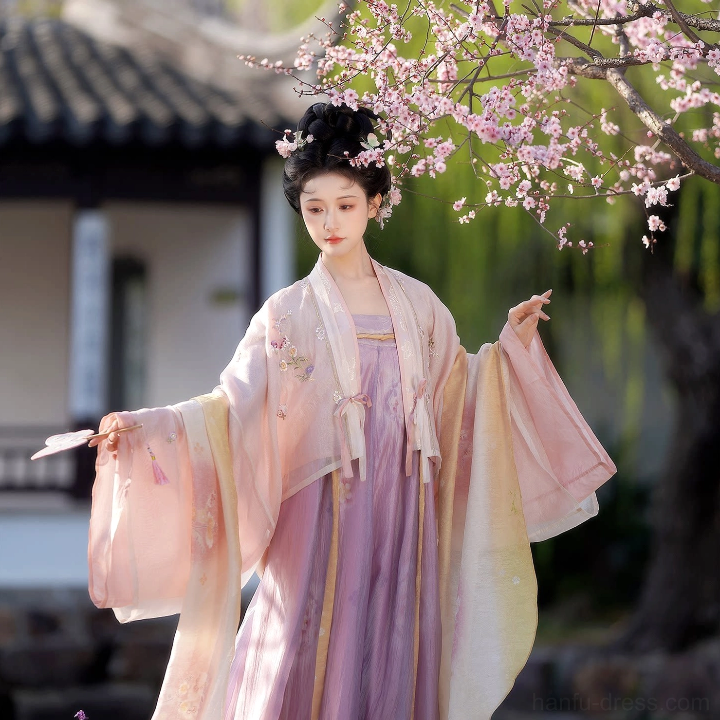 Full-length traditional Tang Dynasty hanfu set featuring wide flowing sleeves, subtle floral embroidery, pastel pink cardigan and lavender qixiong skirt in a Chinese courtyard