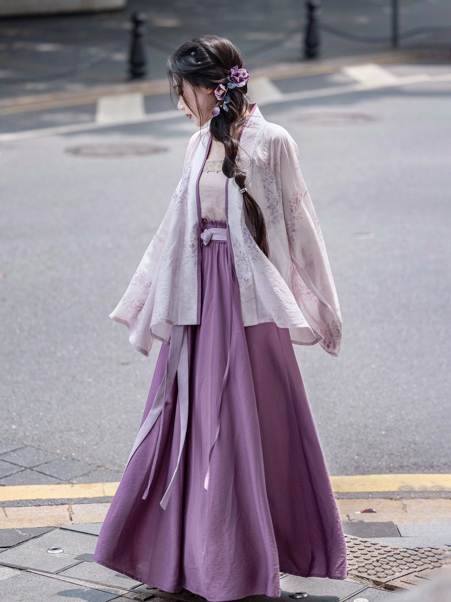 Back three-quarter view of a wisteria themed Song Dynasty Hanfu outfit with a sheer lavender cardigan, flowing purple skirt, long waist ribbons, and floral hairpin