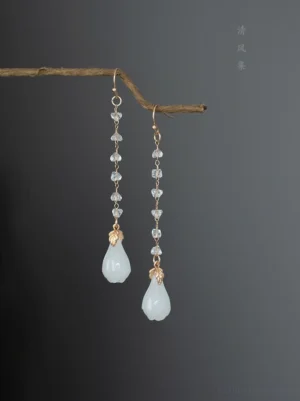 Icy magnolia crystal drop Chinese earrings for Hanfu with milky white jade-like flower pendants, gold leaf accents, and clear faceted crystal chains displayed on a natural twig