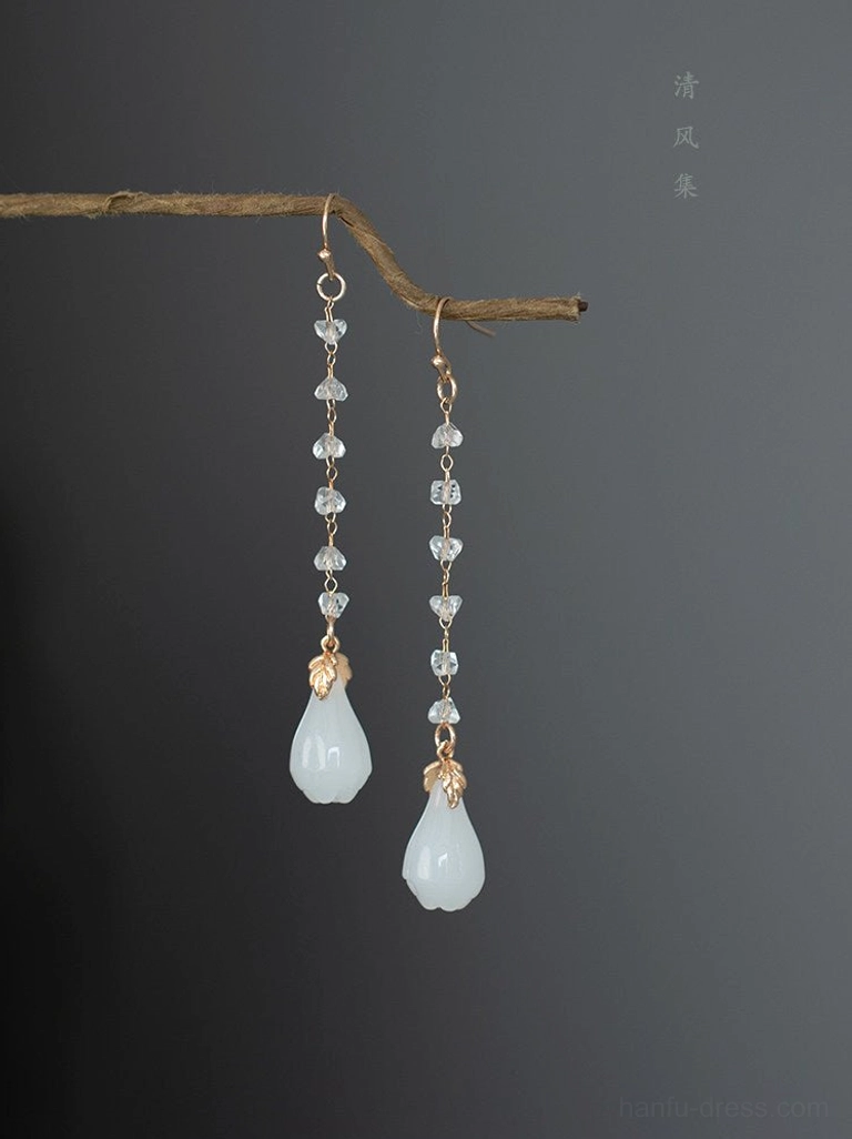 Icy magnolia crystal drop Chinese earrings for Hanfu with milky white jade-like flower pendants, gold leaf accents, and clear faceted crystal chains displayed on a natural twig
