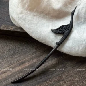 Hand-carved immortal crane Chinese hair stick in matte dark brown wood displayed on a dark wood tabletop with white linen fabric