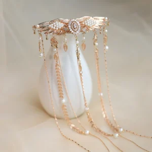 Gold winged tassel hair comb with faux pearls rhinestones and cascading chain pendants displayed against a soft beige backdrop