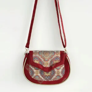 Front view of a wine red imperial brocade Chinese crossbody saddle bag with gold tone trim, central floral mandala medallion, and matching woven jacquard shoulder strap