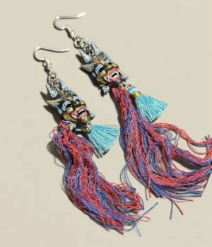 Pair of Chinese imperial lion mask tassel drop earrings in flat lay, with colorful painted lion charms, silver hooks, red blue and cyan tassels