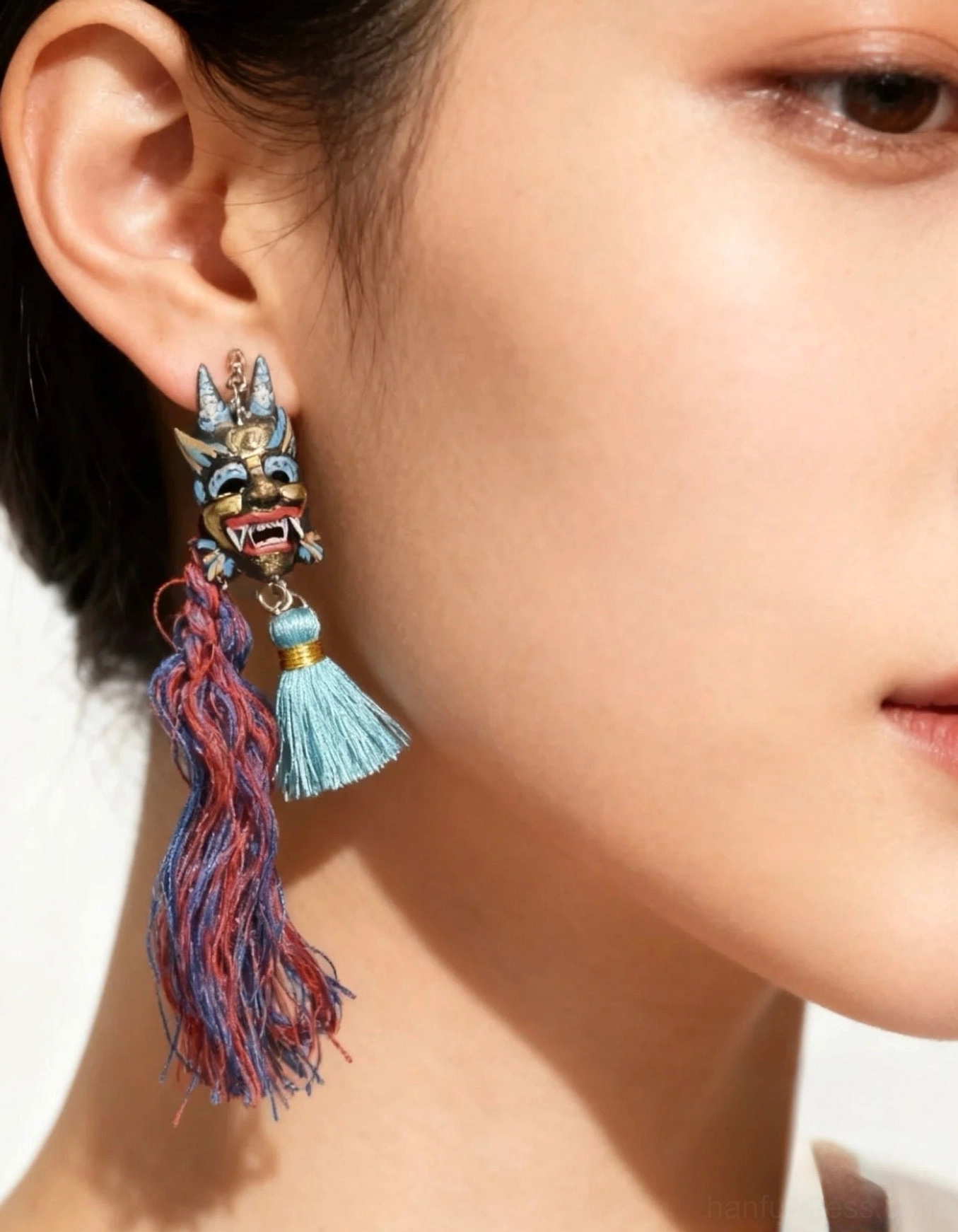 Chinese imperial lion mask tassel hook earrings worn on ear, featuring hand-painted folk lion charm with red blue and cyan tassels