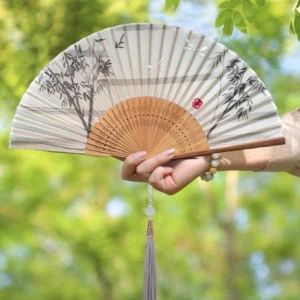 Ink bamboo Chinese folding hand fan with carved wooden ribs, gray purple tassel, and red seal accent held outdoors