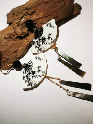 Black and white bamboo fan-shaped Chinese drop earrings displayed on weathered driftwood with black beads, gold ear hooks, and long dual-tone metal tassels
