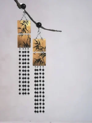 Asymmetrical ink bamboo square tassel Chinese earrings with black beads and silver tone chains displayed on a dry branch