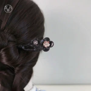 Traditional Chinese wooden Hanfu hair stick in a styled braided updo with two delicate plum blossom flowers, metallic details, and gemstone centers