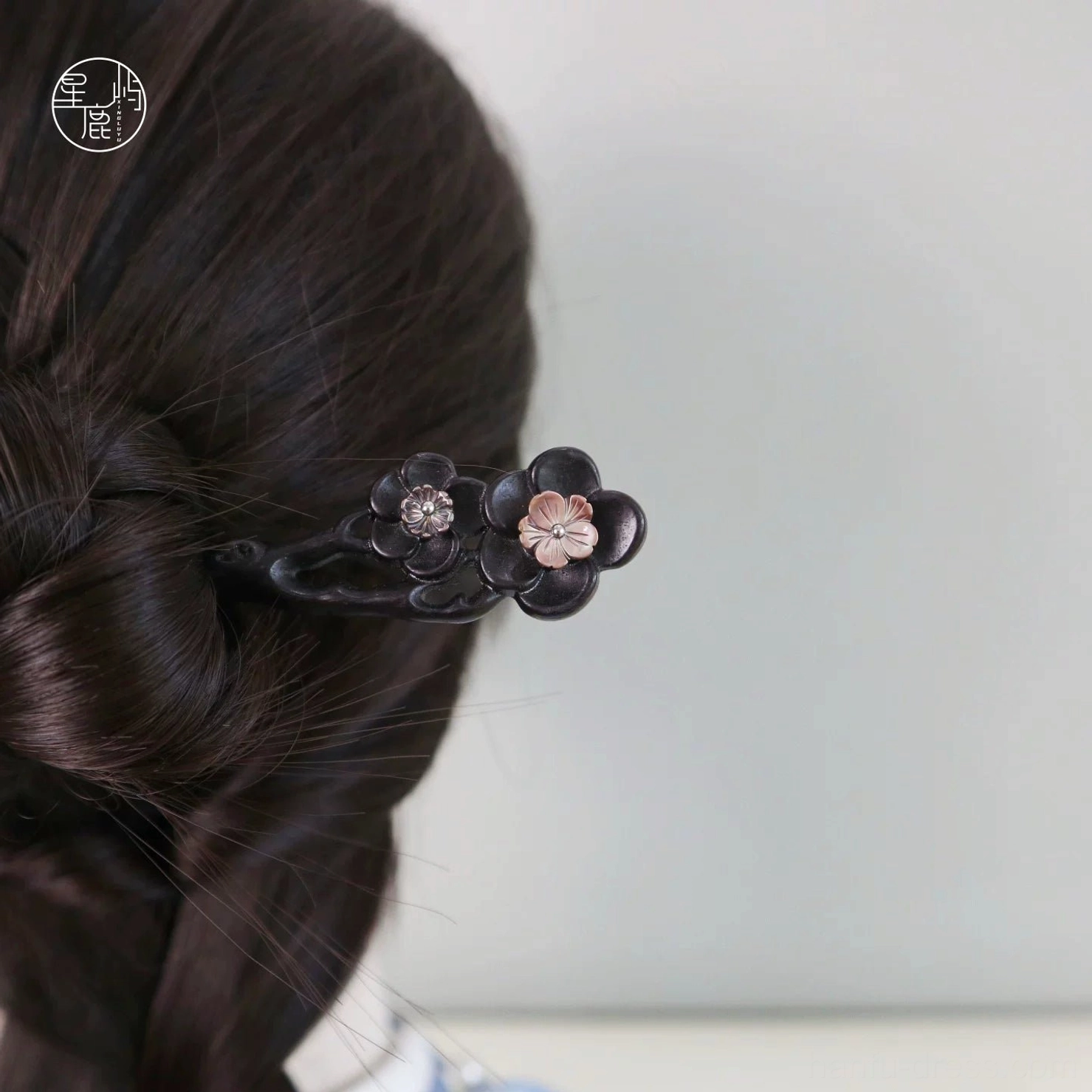 Traditional Chinese wooden Hanfu hair stick in a styled braided updo with two delicate plum blossom flowers, metallic details, and gemstone centers