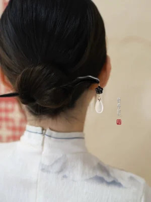 Traditional Chinese hair stick worn in a sleek low bun, showing the dangling white pendant at the back of the hairstyle