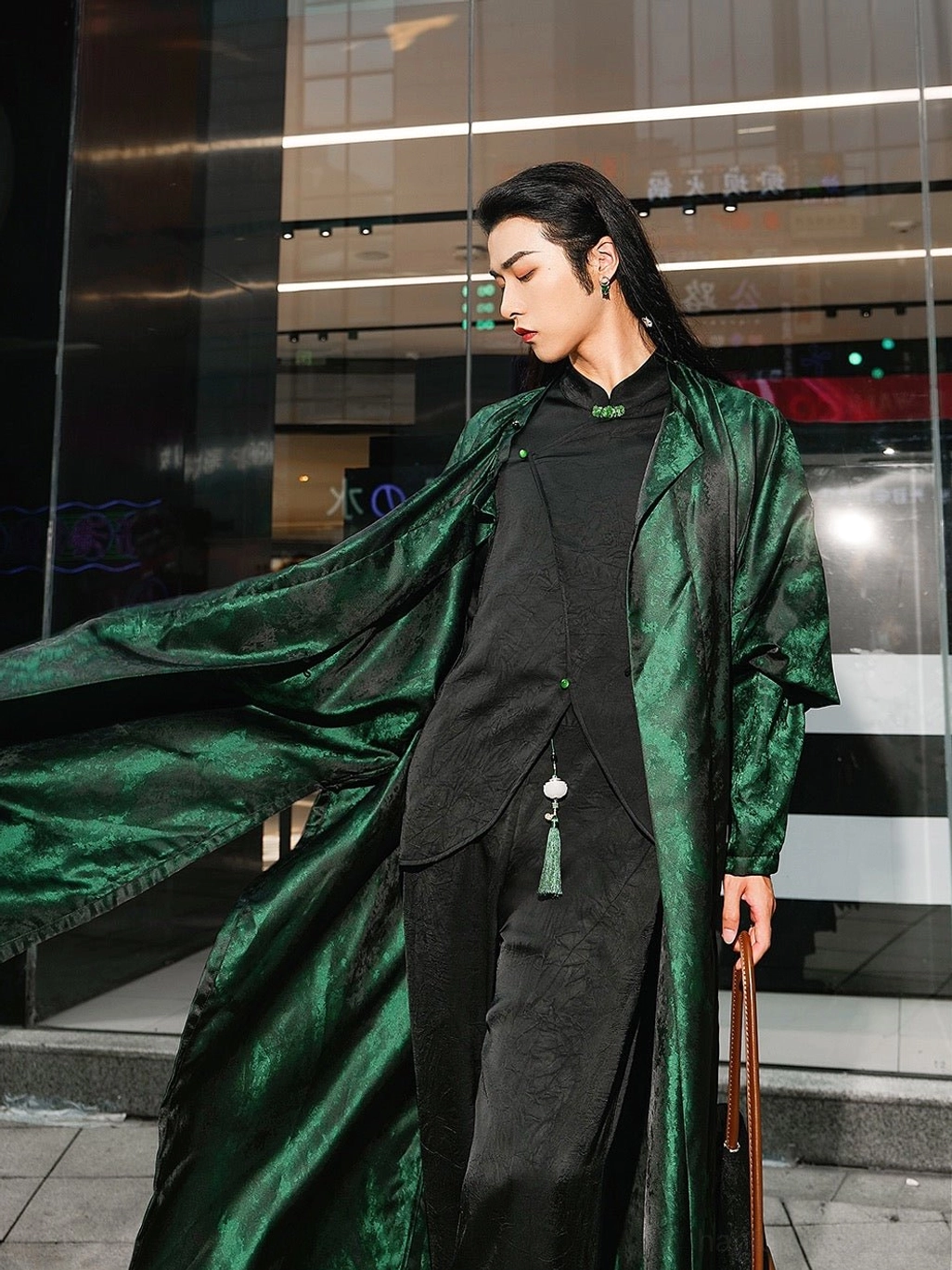 Side view of a model wearing the flowing Ink River green Tang Dynasty Hanfu robe over a black inner outfit, with long fluttering hem, tassel pendant, and contemporary leather handbag