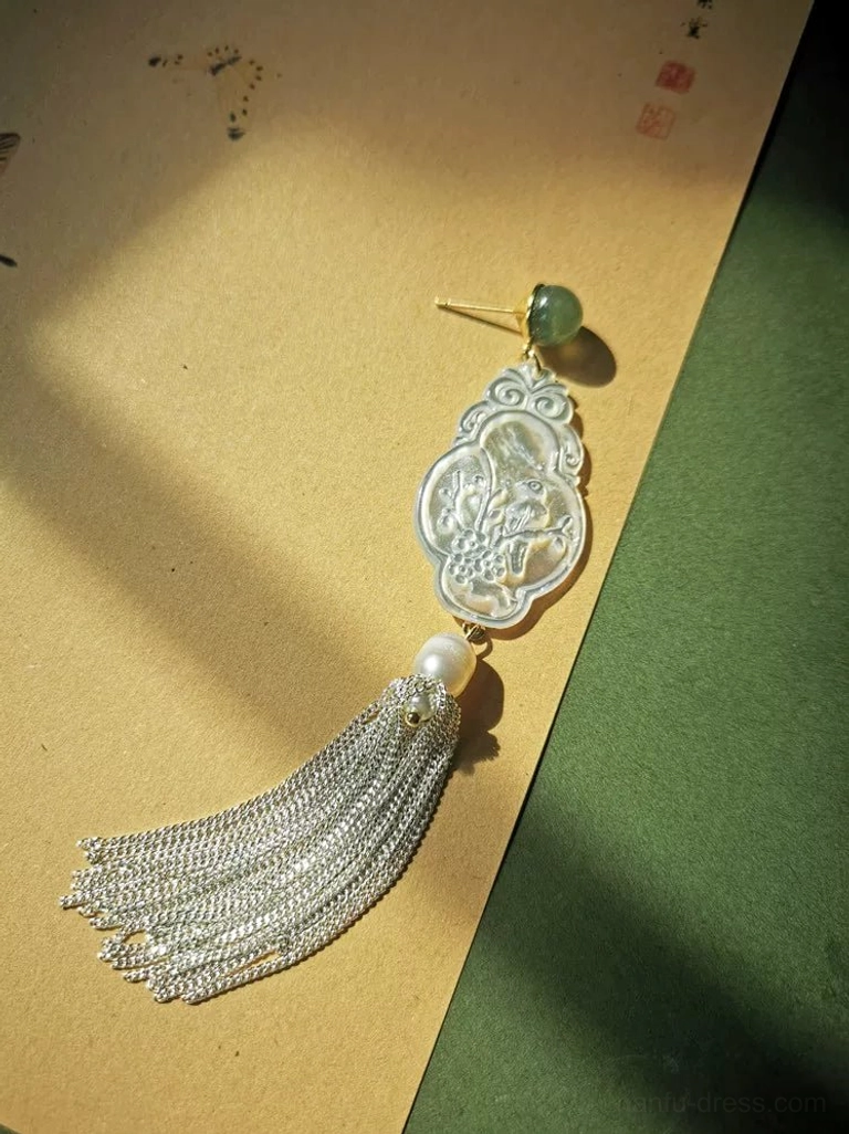 Single iridescent carved shell Hanfu earring with silver chain tassel, pearl, and green jade stud on vintage paper