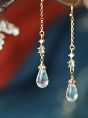 Gold-tone Hanfu crystal drop earrings with iridescent glass teardrop pendants displayed against dark blue and red fabric
