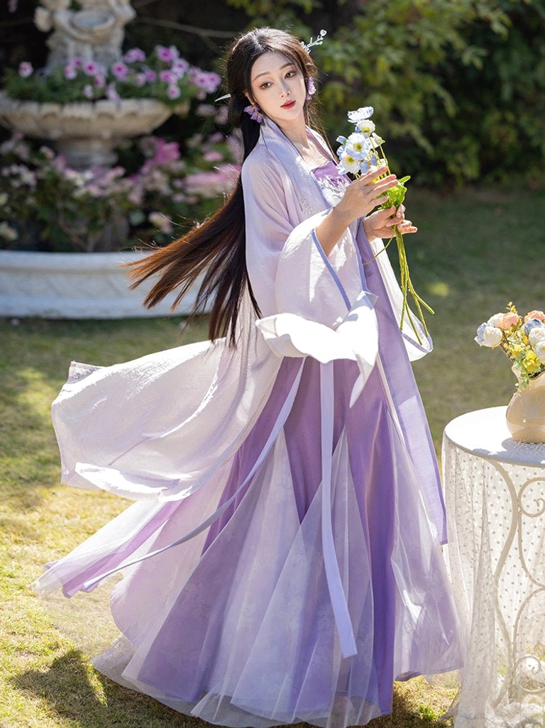 Rear three-quarter view of iris purple Song style Hanfu with sheer flowing wrap skirt and long lavender fairy cardigan outdoors