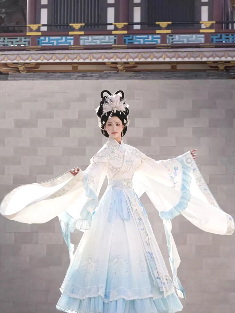 Front three-quarter view of ivory and light blue Wei Jin Dynasty Hanfu with cross-collar top, layered embroidered skirt, and wide ruffled sleeves