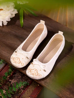 Ivory cloud embroidered Hanfu shoes for women with golden toe embroidery bow ornament and breathable woven insoles displayed on a dark wooden table