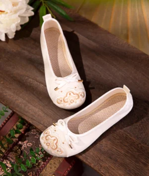 Pair of ivory traditional Chinese Hanfu cloth flats with gold auspicious cloud embroidery and bow decorations styled with Chinese decorative props