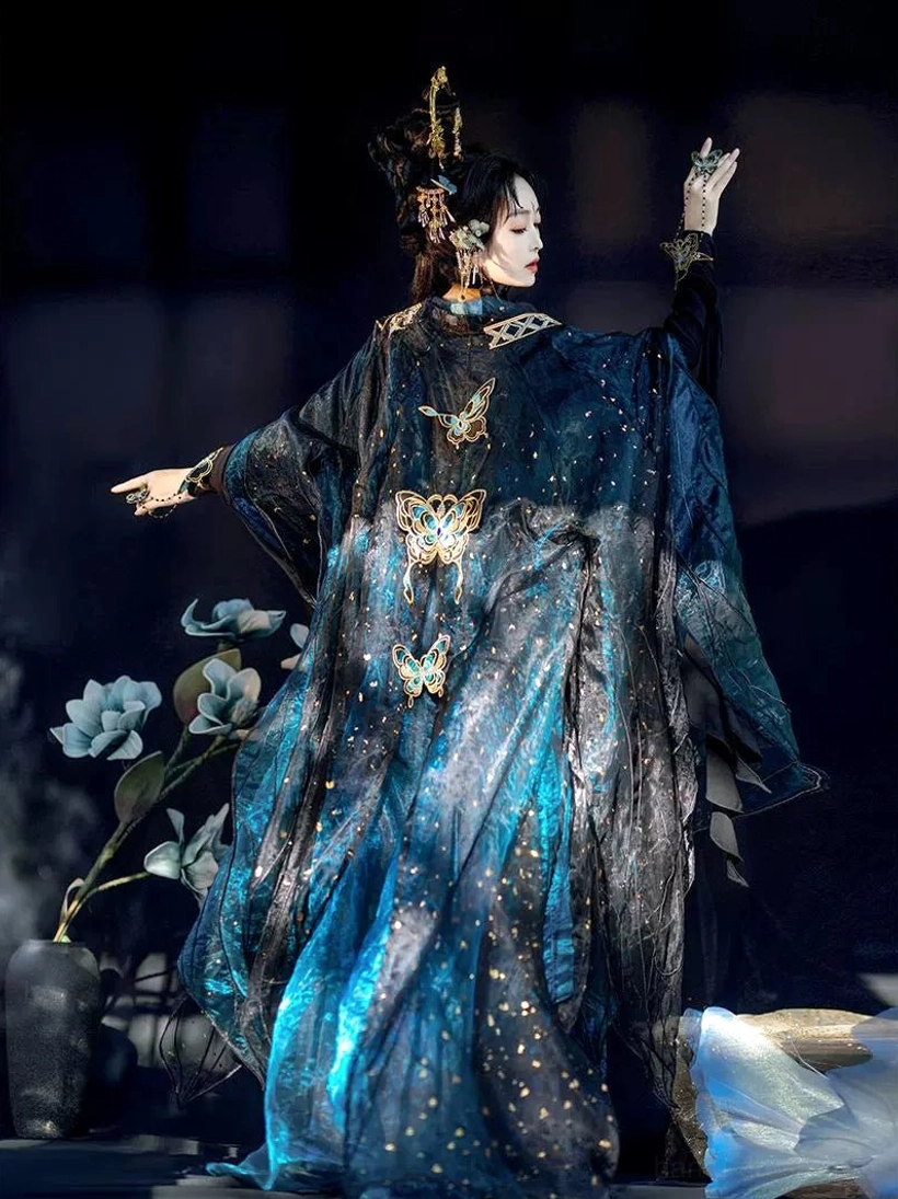 Back three-quarter view of a woman in Tang Dynasty style Hanfu with golden butterfly embroidery, matching cuffs, wide outer sleeves, and sparkling blue-black gradient skirt