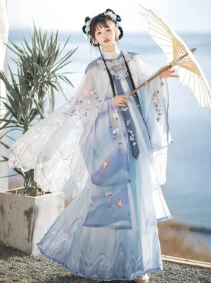 Light blue Jade Butterfly Ming Dynasty Hanfu set with sheer gradient fairy cloak, embroidered wide sleeves, pleated skirt, and cloud collar styled with a traditional paper oil-paper umbrella