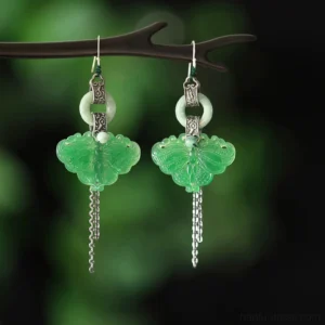Vintage jade butterfly tassel earrings displayed on a wooden jewelry stand with green foliage background, Chinese cheongsam jewelry design
