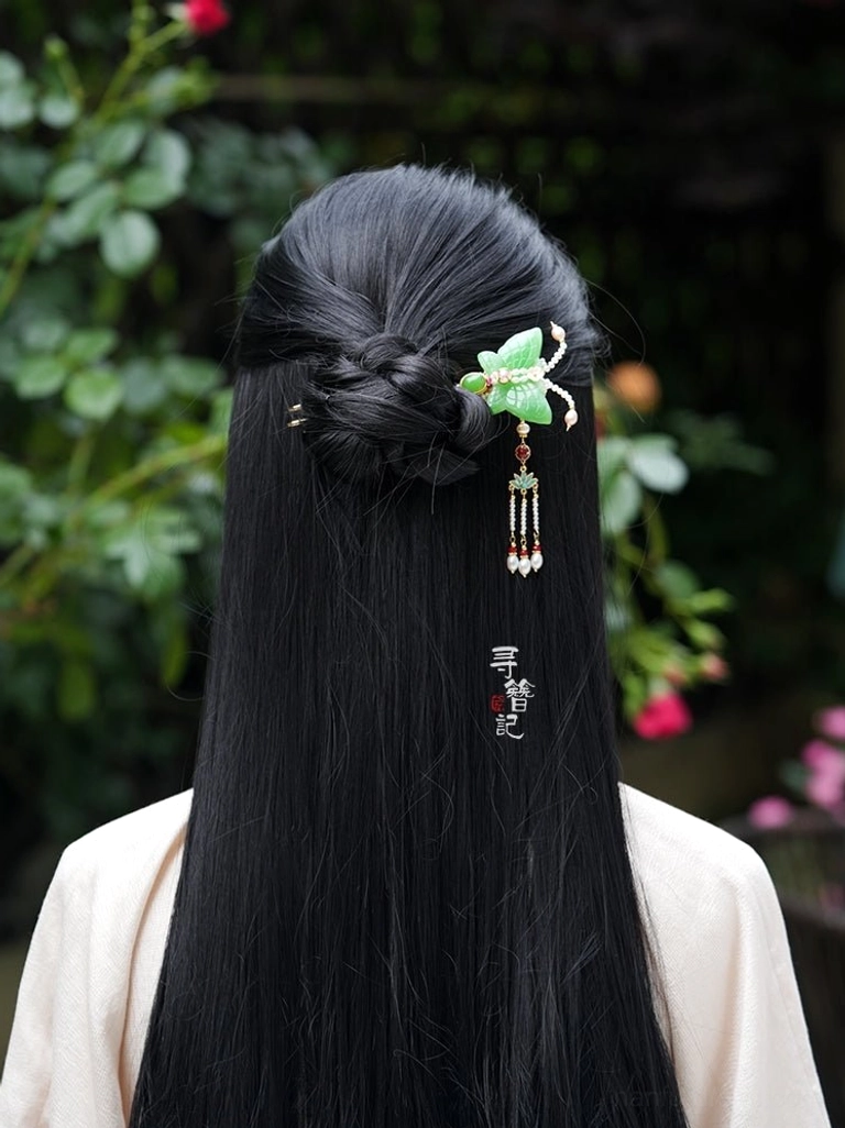Woman wearing a traditional Chinese butterfly pearl tassel hair pin with a braided Hanfu hairstyle against a green garden background