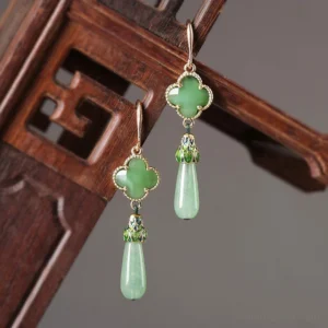 Light green jade four-leaf clover drop earrings with gold-toned trim, enamel accents, and teardrop pendants displayed on Chinese vintage wooden decor