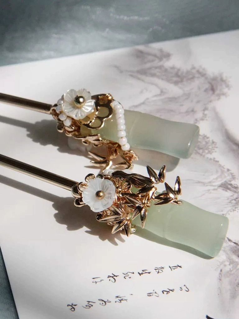 Jade green bamboo Chinese hair sticks with gold leaf floral ornaments displayed on traditional calligraphy paper