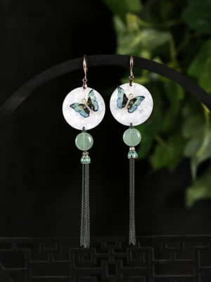 Butterfly tassel Cheongsam earrings hanging on a black display stand with green plants and Chinese style background