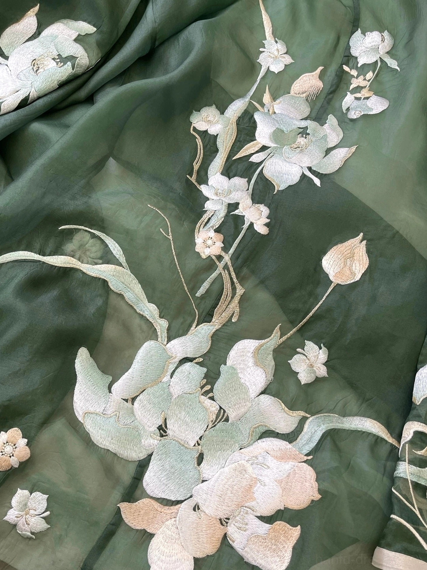 Close-up overhead view of dark olive green Hanfu chiffon fabric featuring detailed ivory and beige lotus flowers, buds, leaves, and decorative floral embroidery