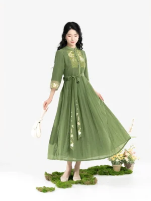 Front full-body view of a jade green Chinese-inspired Tencel pleated dress with matching waist belt, embroidered sash pendant, stand collar, and elegant flowing skirt