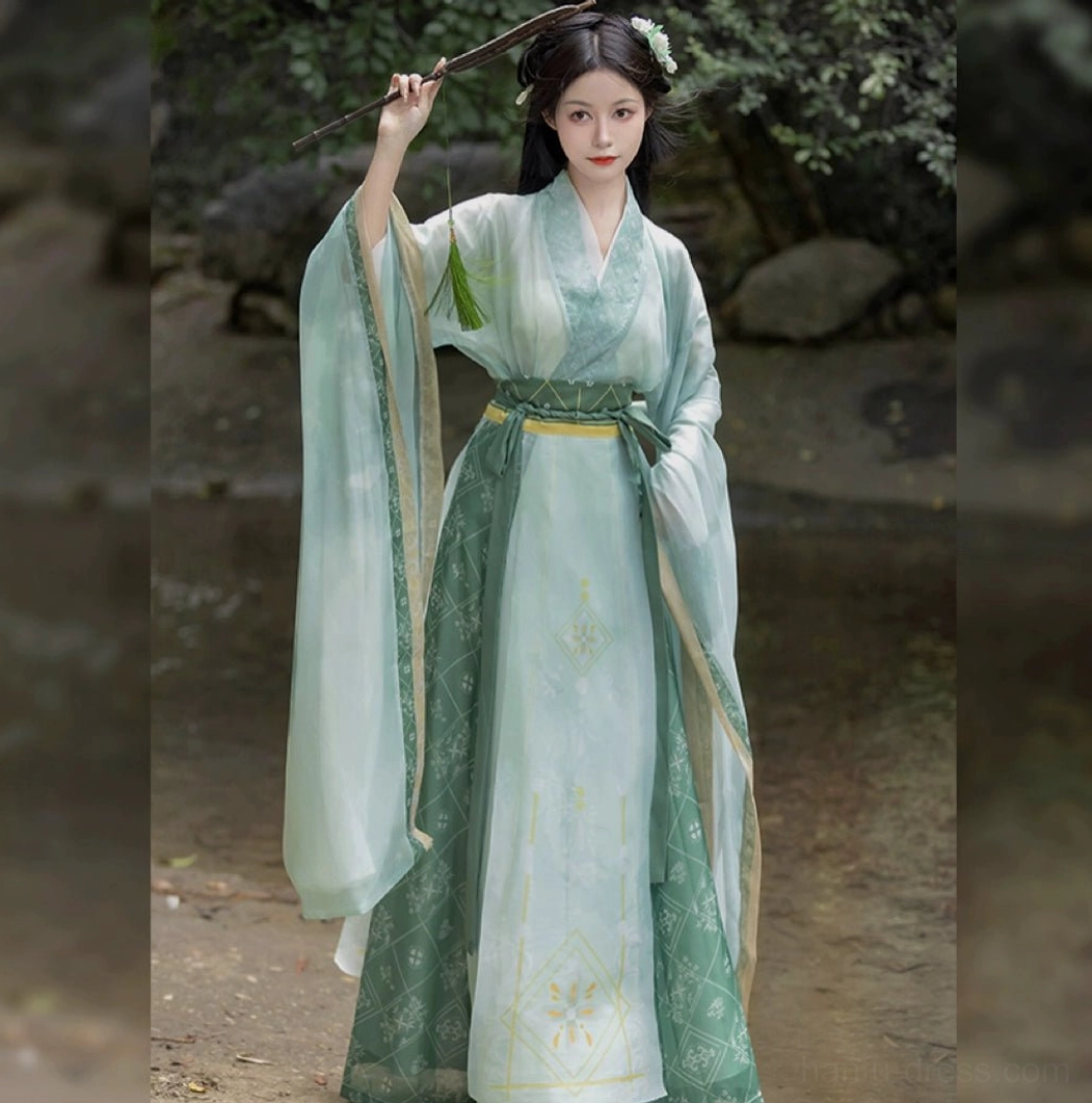 Three-quarter front view of a jade-green Wei Jin style Ruqun Hanfu with cross-collar neckline, flowing wide sleeves, matching waistband, and traditional green tassel prop