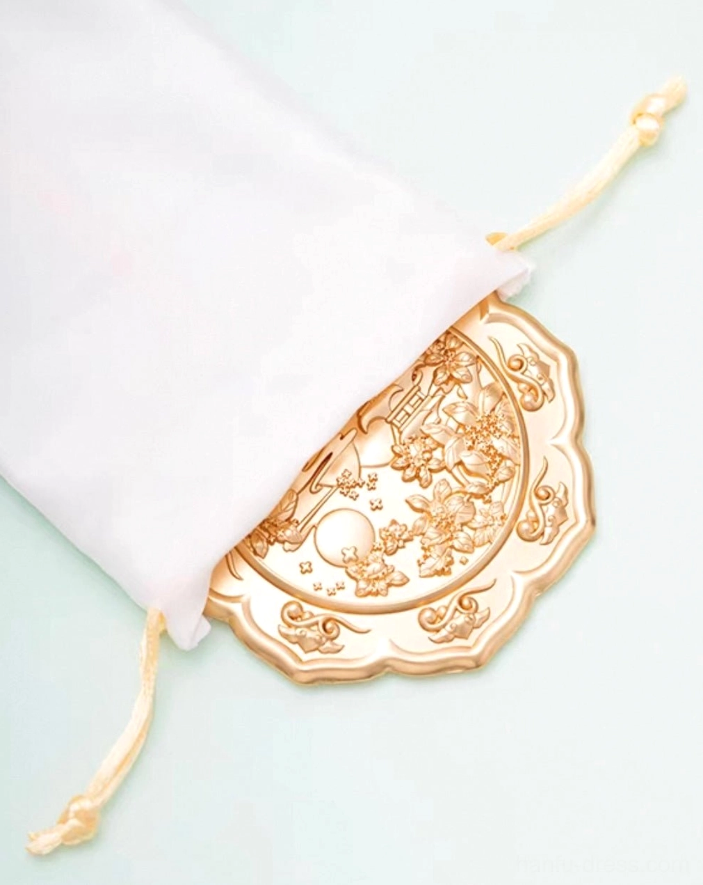 Jade Rabbit Chinese hand mirror resting inside a beige drawstring velvet pouch, showing its rose gold embossed moon palace and floral design
