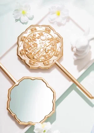 Jade Rabbit Moon Palace Chinese hand mirror shown from above with rose gold scalloped floral frame, embossed reverse, mirrored front, white flowers, and ceramic rabbit decoration