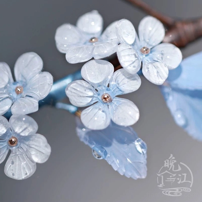 Close-up of translucent white plum blossom petals, gold flower centers, and dewy blue leaves on Chinese hair stick