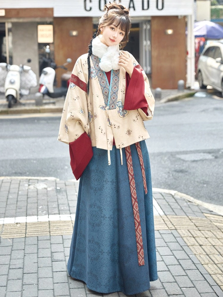 Beige Jin Dynasty inspired modern hanfu jacket and navy skirt outfit with geometric trim, layered red sleeves, waist sash, and white neck warmer worn outdoors