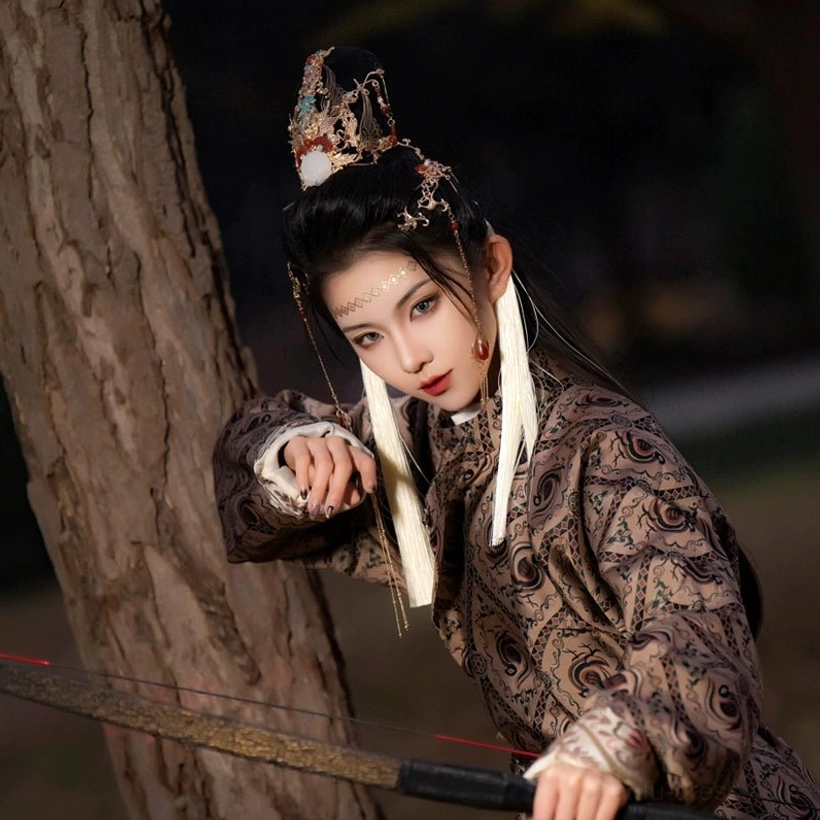 Female model wearing an ornate Jiugao hanfu hair accessories set with gold-tone Chinese hair crown white silk tassels forehead jewelry and dark traditional Hanfu in a woodland setting