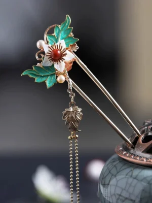 Gold tone Chinese hair stick with white flower green enamel leaves faux pearls and maple leaf tassel displayed on a celadon incense burner