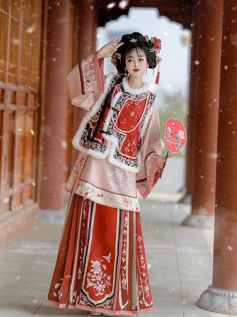 Late Qing Dynasty Han women winter outfit in pink red and beige with embroidered vest floral skirt and plush collar trim in a snowy traditional courtyard
