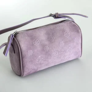 Three-quarter front view of a lavender Chinese barrel crossbody bag with embossed floral suede texture, top zipper closure, leather zipper pull, and matching shoulder strap