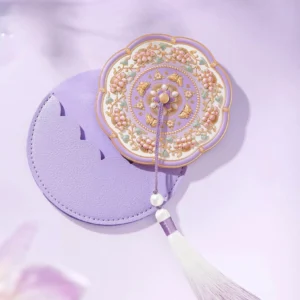 Lavender Chinese pocket mirror with matching matte purple leather storage pouch, scalloped cutout, decorative tassel, and floral embossed design on a soft pastel background