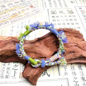 Lavender handwoven Tibetan-inspired knot bracelet with blue green mixed cords and frayed tassel displayed on rustic wood and Chinese calligraphy paper