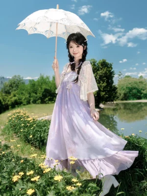Front view of a lavender purple modern Tang-style Hanfu dress with floral chiffon skirt and white lace cropped cardigan in a sunny lakeside flower field