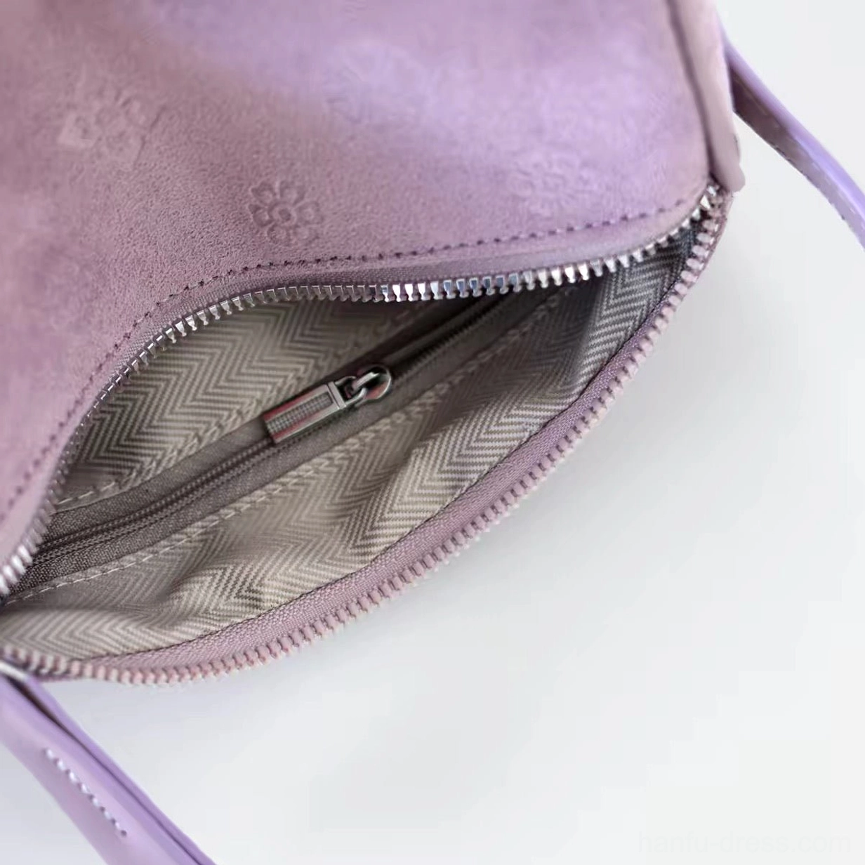 Close-up of lavender suede Chinese crossbody bag open at the top showing silver zipper, leather pull tab, herringbone lining, and inner zipper pocket