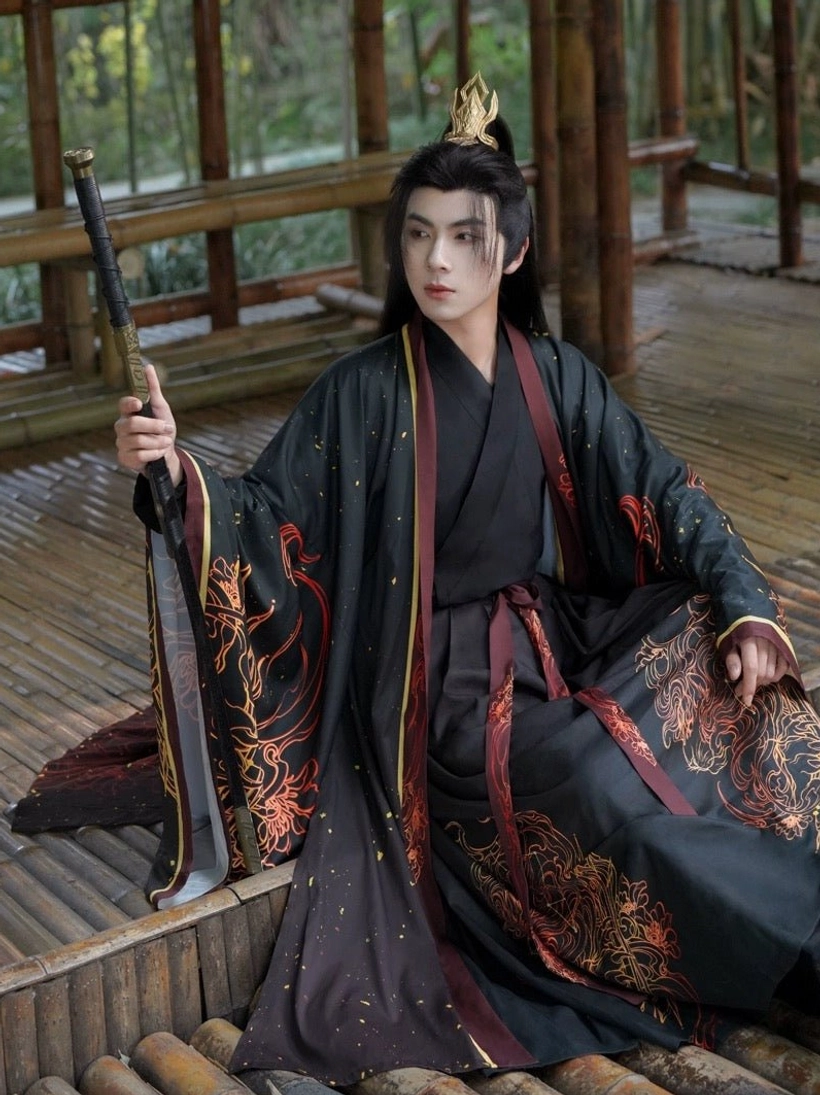 Three-quarter view of a Leo-themed male Hanfu outfit with intricate red and gold flame-inspired motifs, black fabric with subtle gold flecks, and a traditional cross-collar inner top
