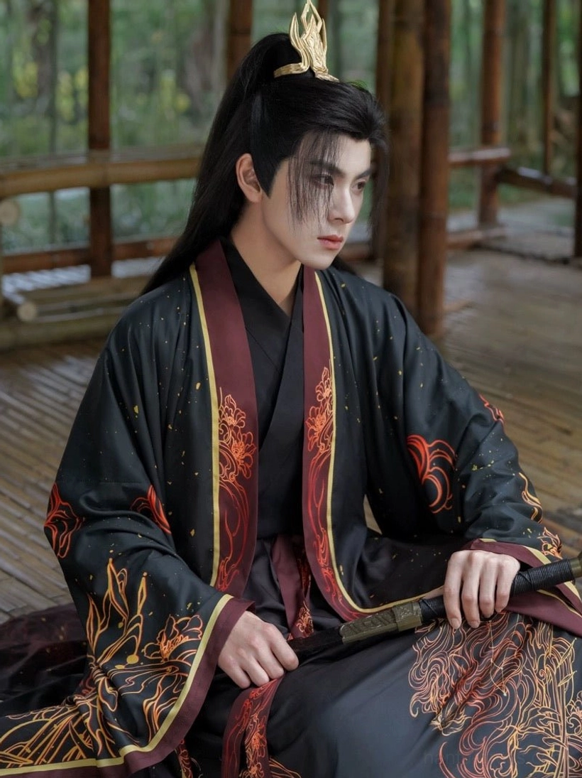 Close front view of a male Leo-style Wuxia Hanfu showing the cross-collar construction, maroon and gold robe edging, decorative sleeve motifs, and layered skirt panels