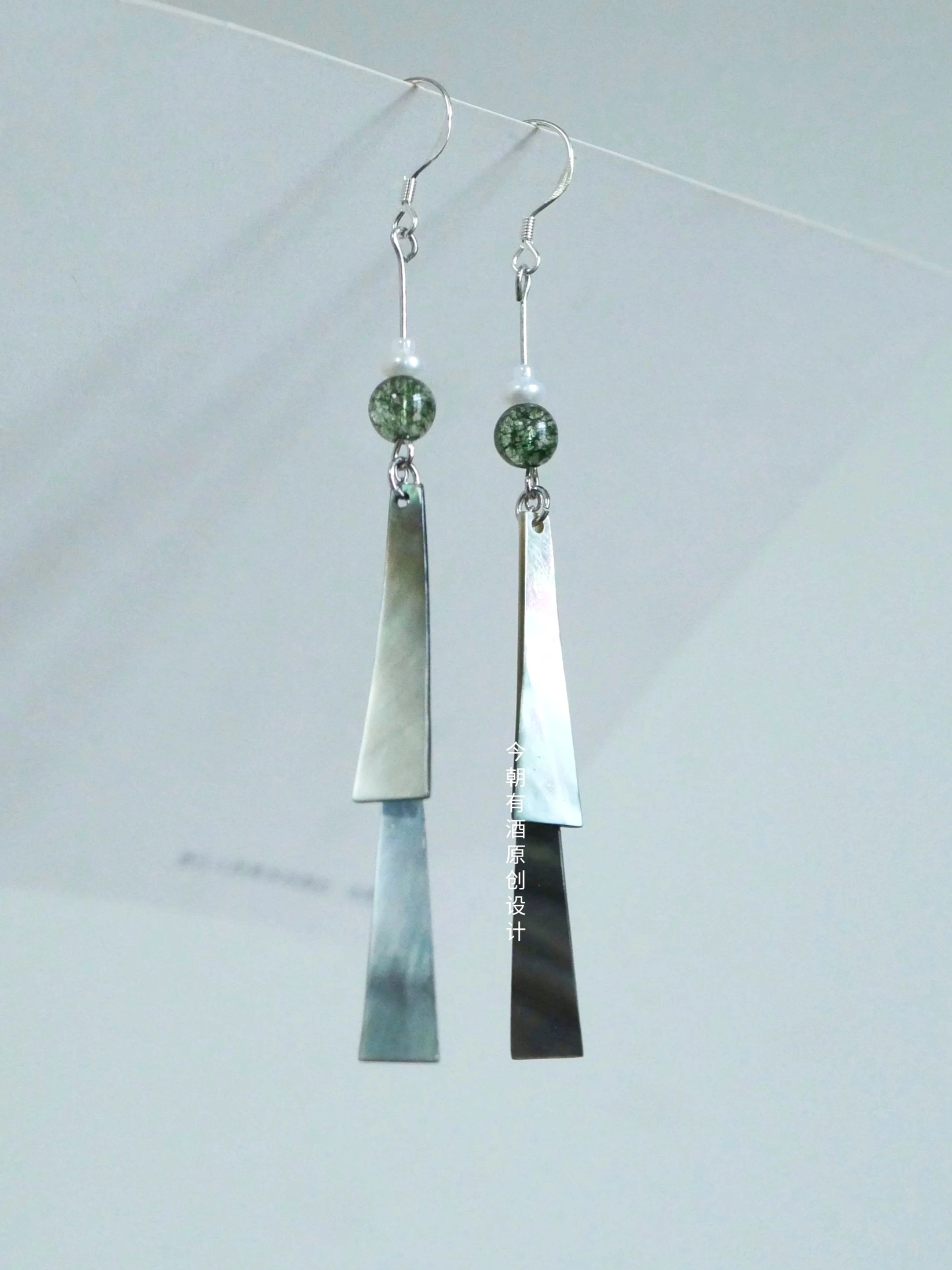 Traditional Chinese style hook earrings with green speckled beads and layered two-tone trapezoid pendants on white display board