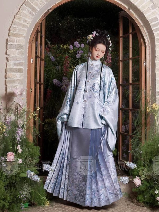 Light blue Chinese Hanfu outfit with floral embroidered standing collar top and pleated mamianqun skirt shown in a traditional garden setting