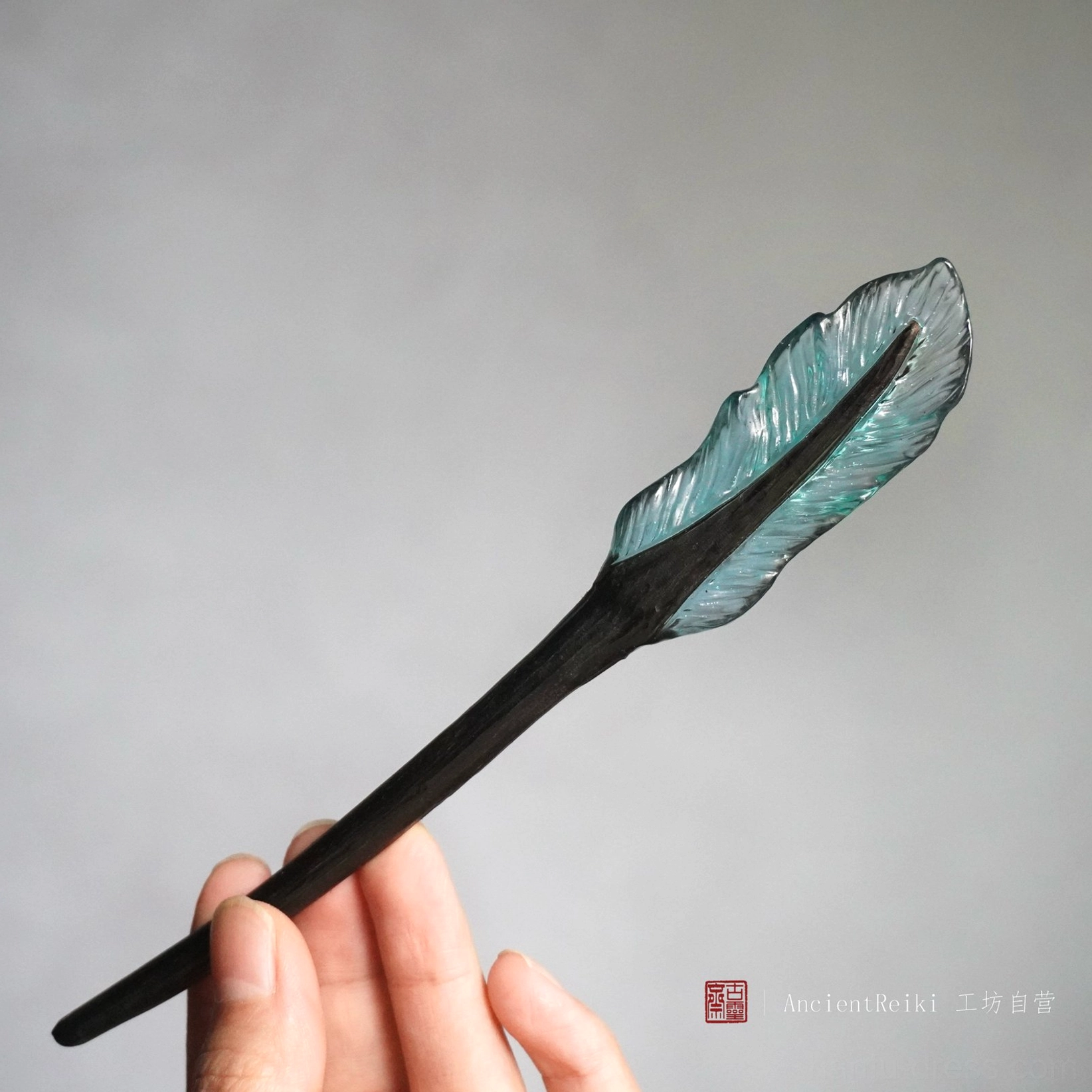 Light blue feather Chinese hair stick close-up with translucent detailed feather top and black wooden pin