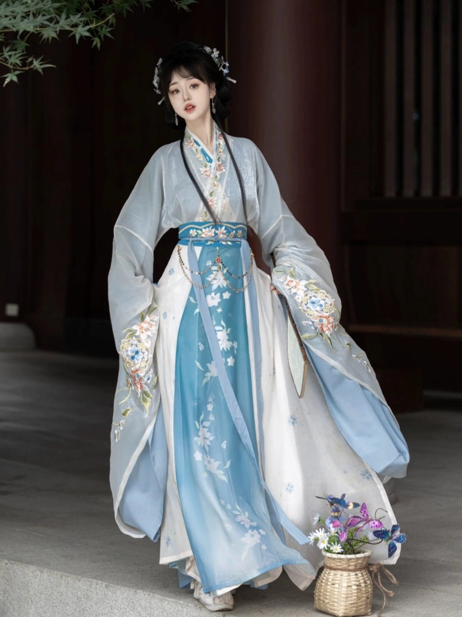 Light blue gradient Wei Jin Dynasty Hanfu three-quarter view with floral wrap skirt, embroidered sleeve cuffs, matching waist sash, and wide flowing sleeves in a wooden corridor